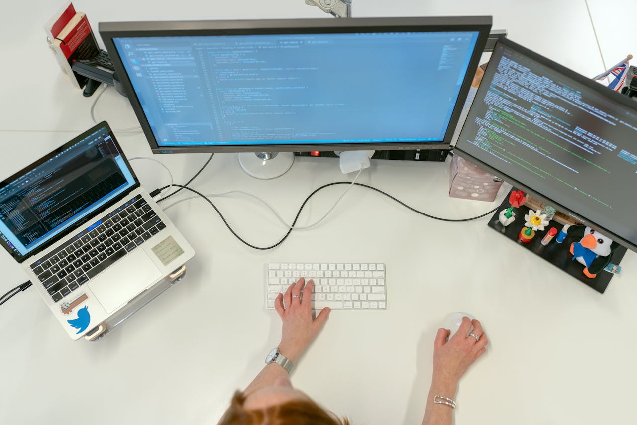 home-img A female software engineer coding on dual monitors and a laptop in an office setting.