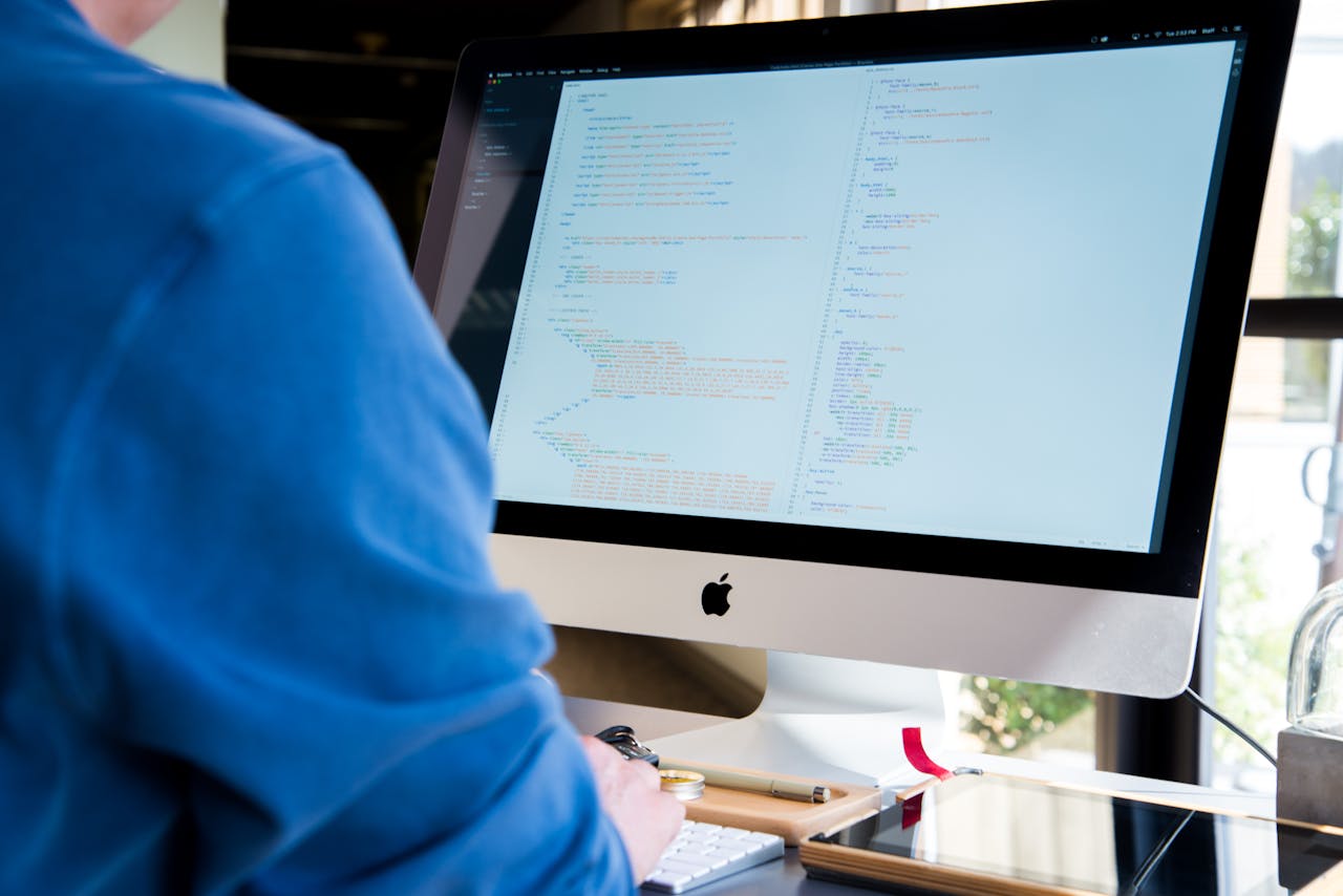 A programmer in a blue shirt coding on an iMac. Perfect for technology or work-related themes.